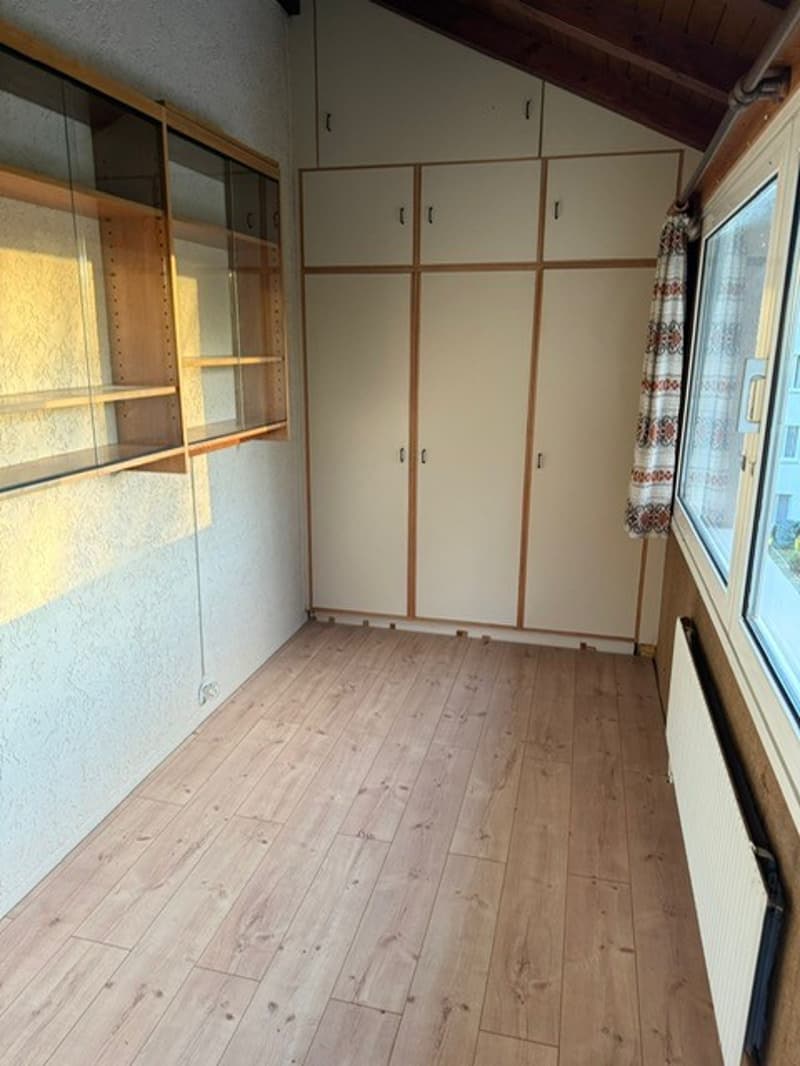 Empty room with wooden floor, built-in cabinets, shelves, window, and radiator.