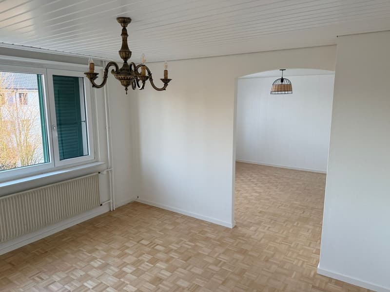 Empty room, wooden floors, white walls, two windows with shutters, radiator, chandelier, small hanging lamp