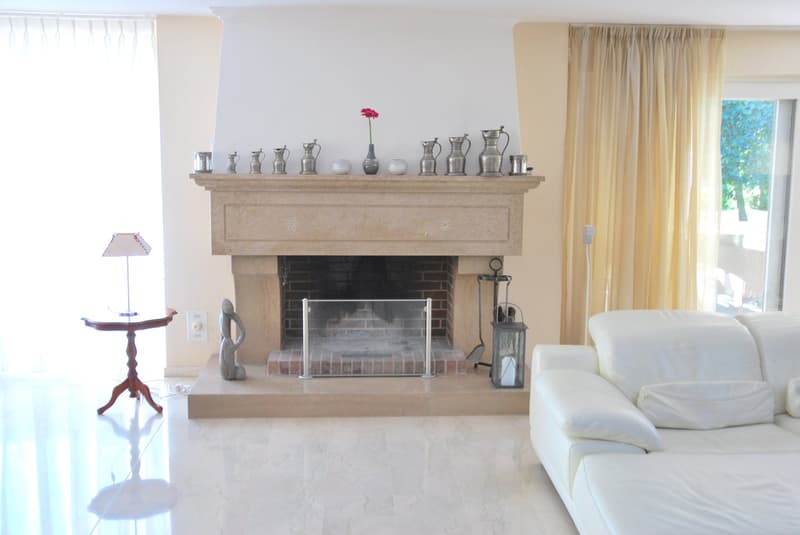 Living room with a white couch, marble floor, fireplace, glass side door, glass window, white curtains, glass table, and a glass lamp