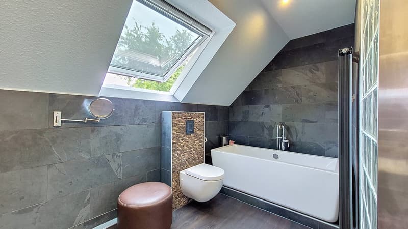 a bathroom with a bathtub, toilet, mirror, and ceiling window