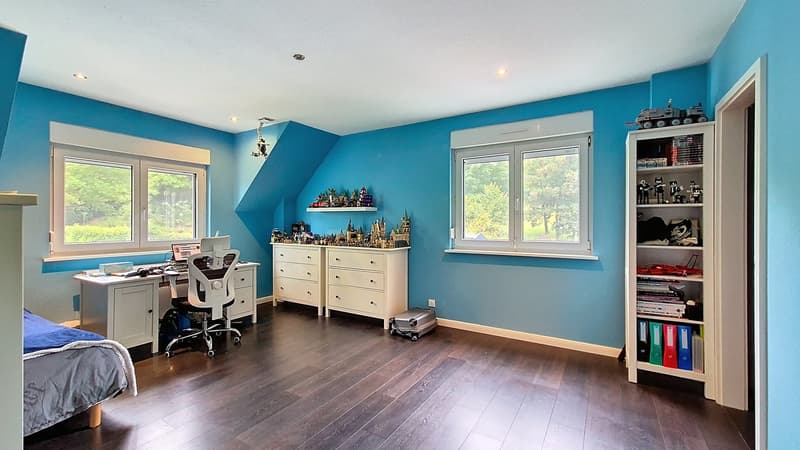 blue walls, wooden floor, bed, desk with computer, chair, cabinet, shelves, book cases, suitcase, toys