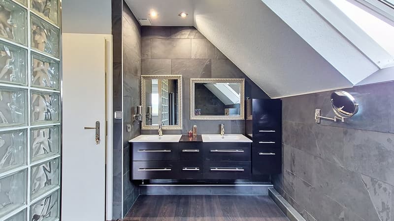 Modern bathroom with a double sink, tiled walls, wooden floor, and skylight