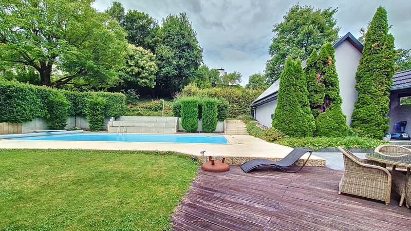 A well maintained garden with a swimming pool, wooden deck, and a view of the trees and landscape