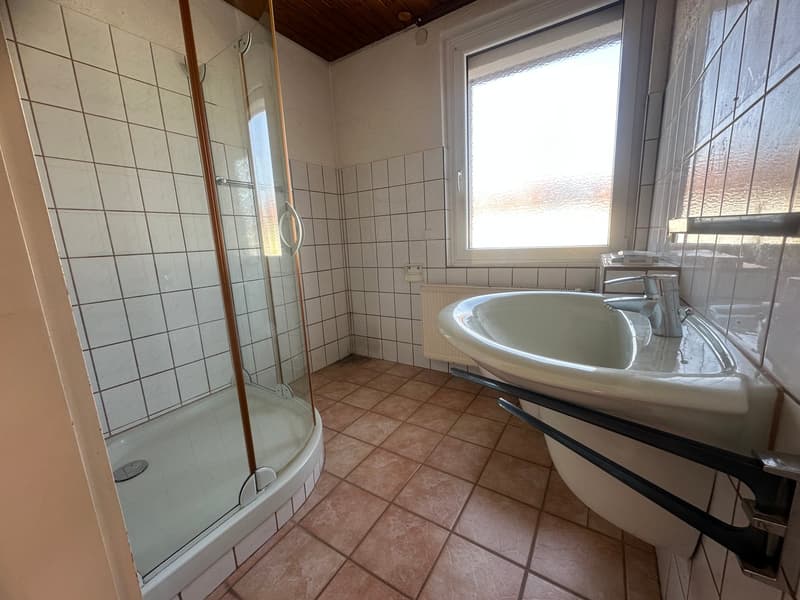 White tiled walls, white tiled floor, shower stall, white sink, glass shower door, white radiator