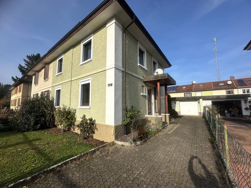 Two-story residential house, yellow and white exterior, garage, fenced garden, brick driveway, solar panels on adjacent building