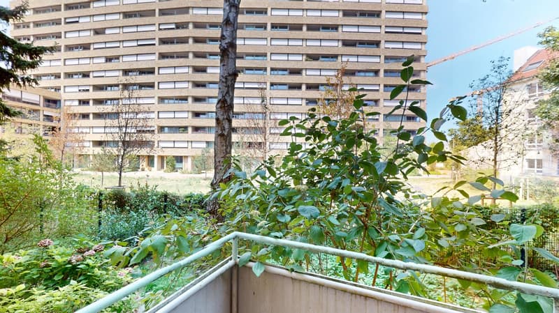 View of a terrace garden with various plants, trees, and shrubs, a tall building in the background, and a crane on the right side