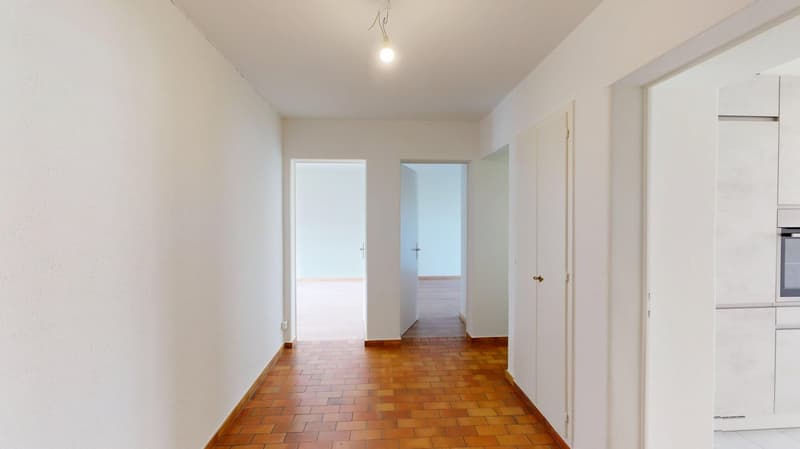 Empty hallway with brick floor, white walls, open doors, and an open ceiling with a light