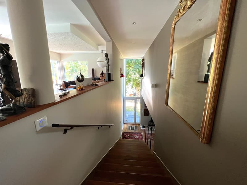 wide wooden stairs, mirror on the wall, decorative items on the shelf, glass door at the end