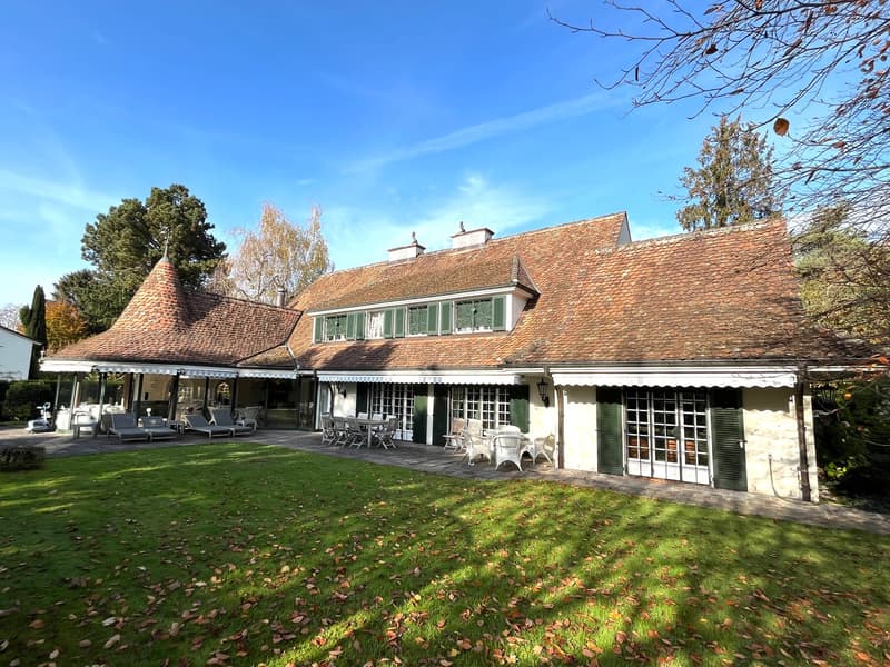 Large house, brown roof, green shutters, covered terrace, outdoor dining area, lawn, trees