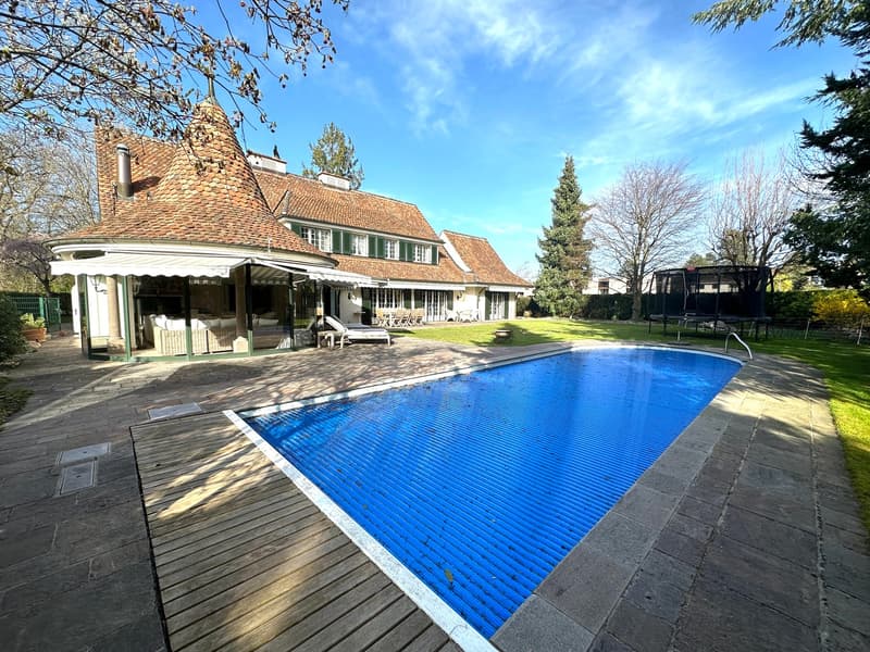 Two story house with brown roof, swimming pool, wooden deck, green lawn, outdoor seating, canopy