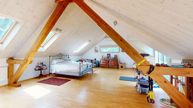 Attic room with slanted wooden ceiling, wooden floor, large bed, wooden stand, windows, wooden cabinet, yoga mat