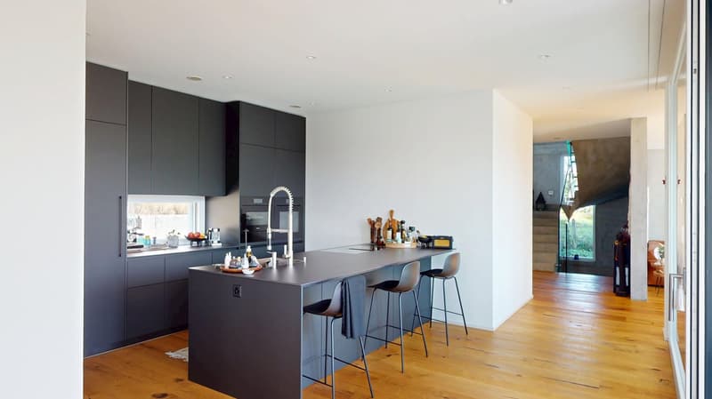 Modern kitchen, island with bar stools, built-in appliances, black cabinets, wooden floor.