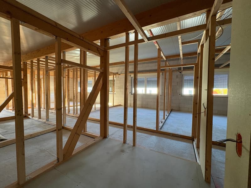 unfinished construction with wooden beams, insulation, open spaces, brick walls, glass windows