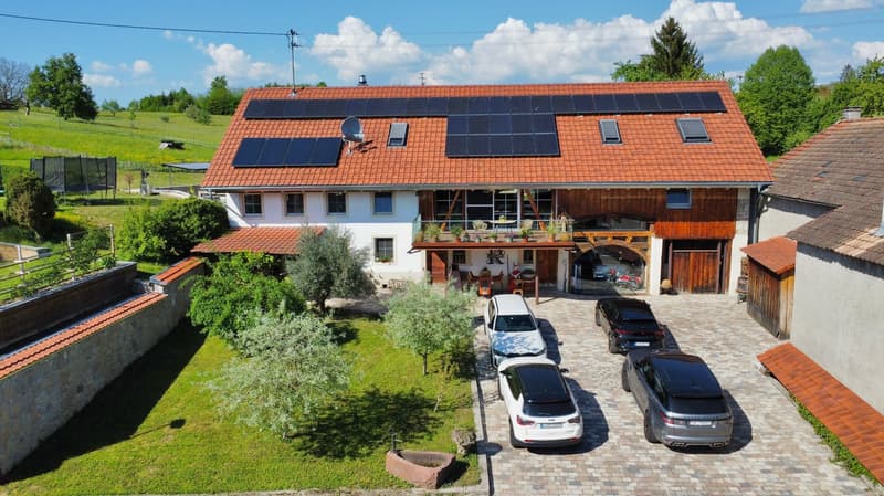 House: Two-story with red roof, multiple solar panels, garage, surrounded by greenery