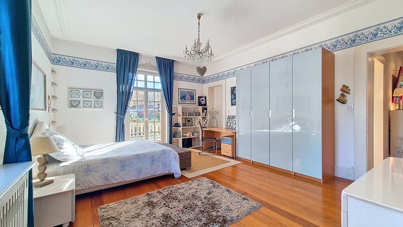 Bed with white bedsheet, lamps, carpet, large wardrobes, shelves, desk, bookshelf, chair