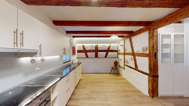 modern kitchen, wooden beams, wooden floors, white walls, built-in cabinets, large countertop, modern stovetop, wooden chair, white shelves