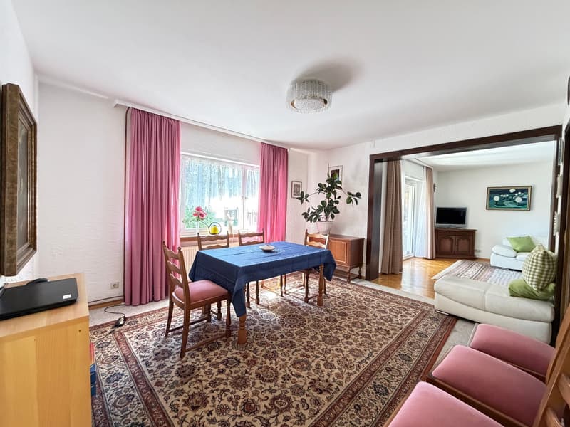 Dining room with a table and chairs, rug, pink curtains, plant, TV, couch, and picture frames