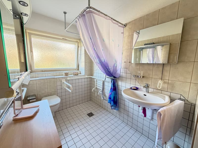 Bathroom with white tiles, white sink, white toilet, shower curtain, mirror, and towel rack.