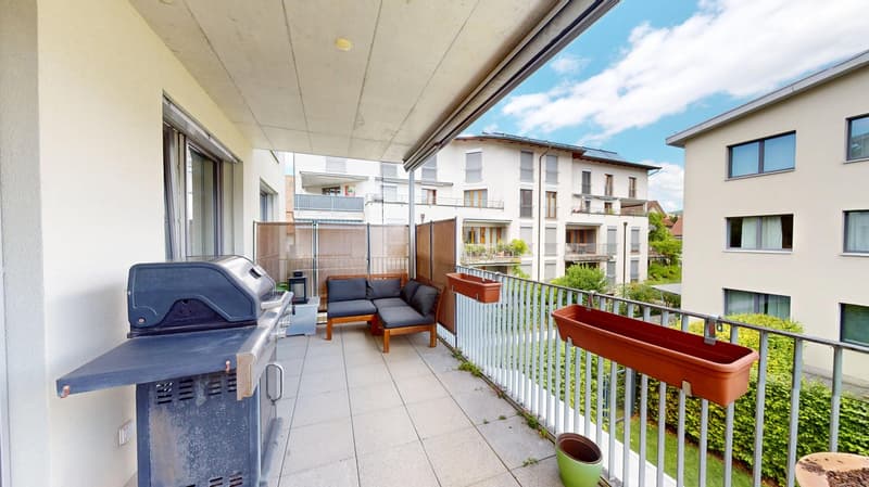 Balcony with a grill, a couch, and a table, with a view of the building