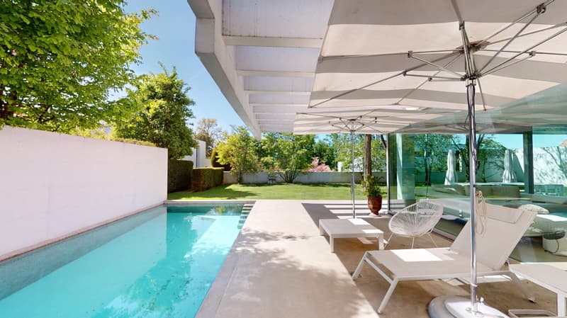 Outdoor area with swimming pool, white lounge chairs, umbrellas, and a table