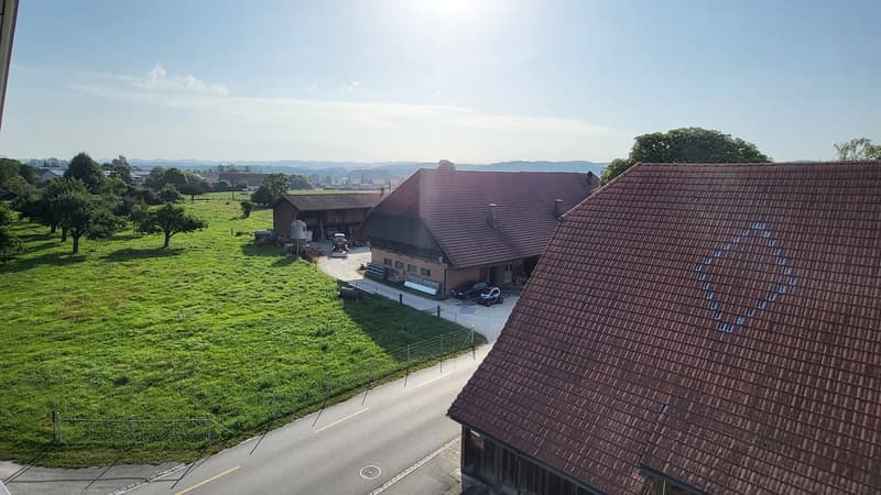 2-story house, red tile roof, driveway with cars parked, grassy field, trees in the background
