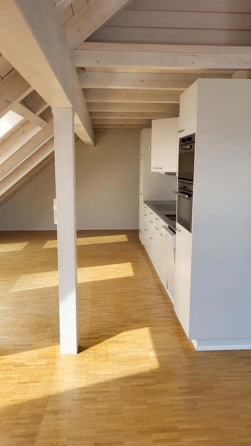 an attic with white walls, wooden floor, wooden beam ceiling, integrated kitchen
