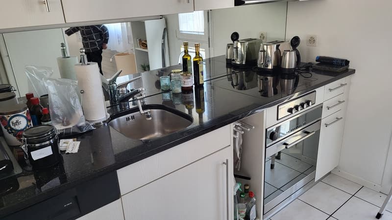 modern kitchen with black granite countertops, stainless steel sink, white cabinets, built-in oven, gas stove, toasters, kettle, and various kitchen utensils and bottles