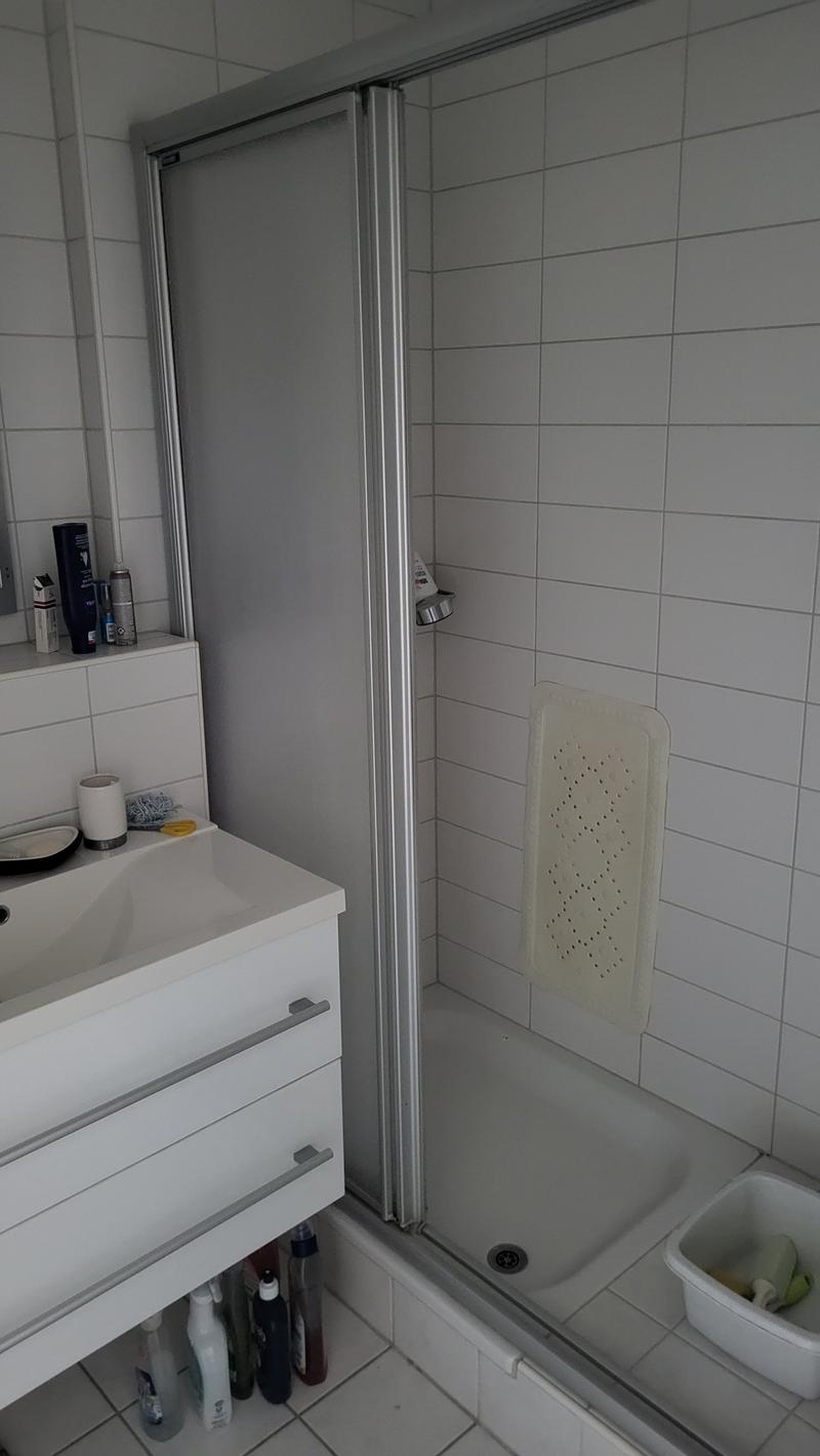 Bathroom with white tiles, shower, sink, and storage cabinet