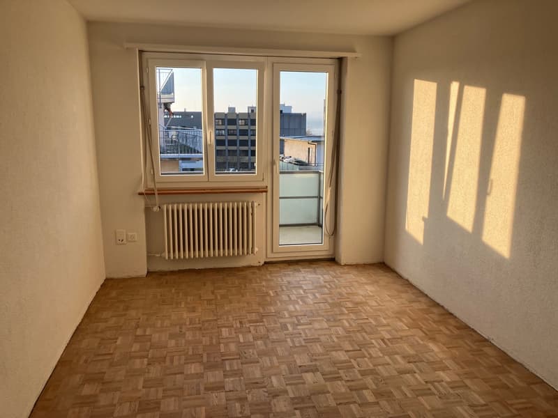 empty room, wooden floor, sliding doors to balcony, view of buildings, radiator