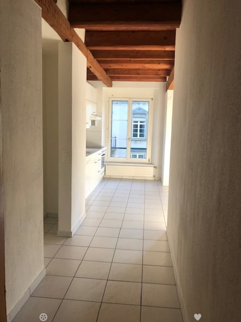 tiled hallway with wooden ceiling beams, kitchen with windows and appliances, small room with an additional window