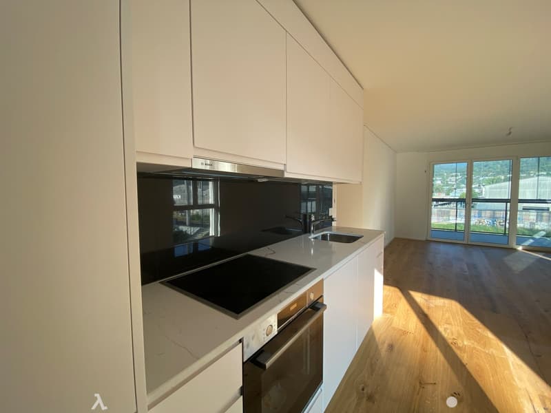 Modern kitchen with a white marble countertop, black induction stove, Bosch kitchen extractor, white wooden flooring, glass doors with view to the outside.