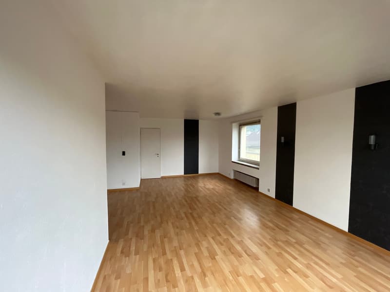 Empty room with white walls, wooden floor, and black accent walls. There are two doors, one of which is open, and a window with a radiator below. Wall-mounted lights are present.