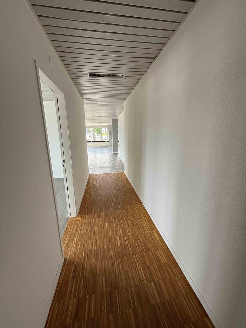Long hallway with white walls, wooden floor, and a ceiling with parallel wooden slats.