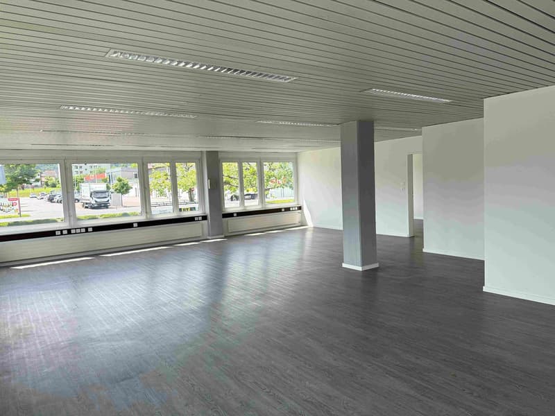 Large open space with high ceilings, gray walls, and a hardwood floor. The space has large windows overlooking the street outside.