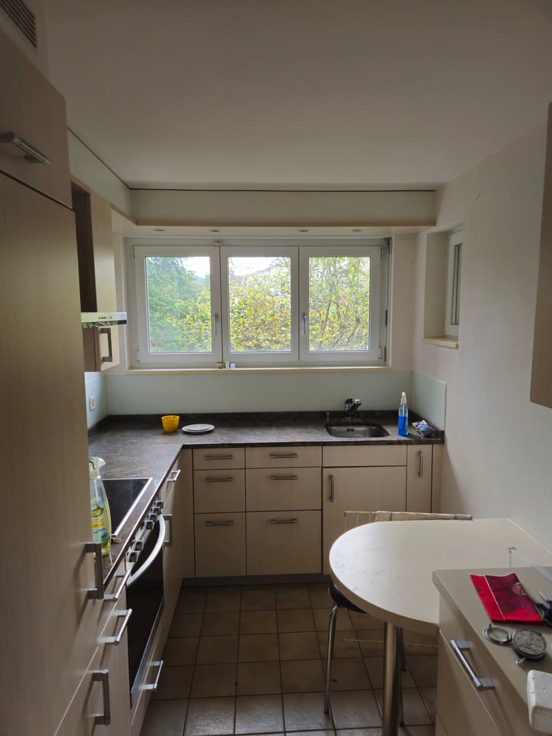 Modern kitchen with large windows, countertop with stove, sink, cabinet space, round table, dishwasher and a bottle on the counter.