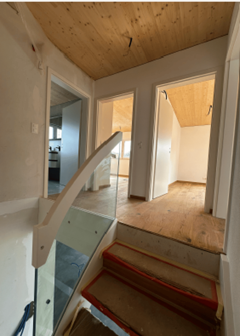 An indoor area showcasing a staircase, with glass handrail and wooden steps.