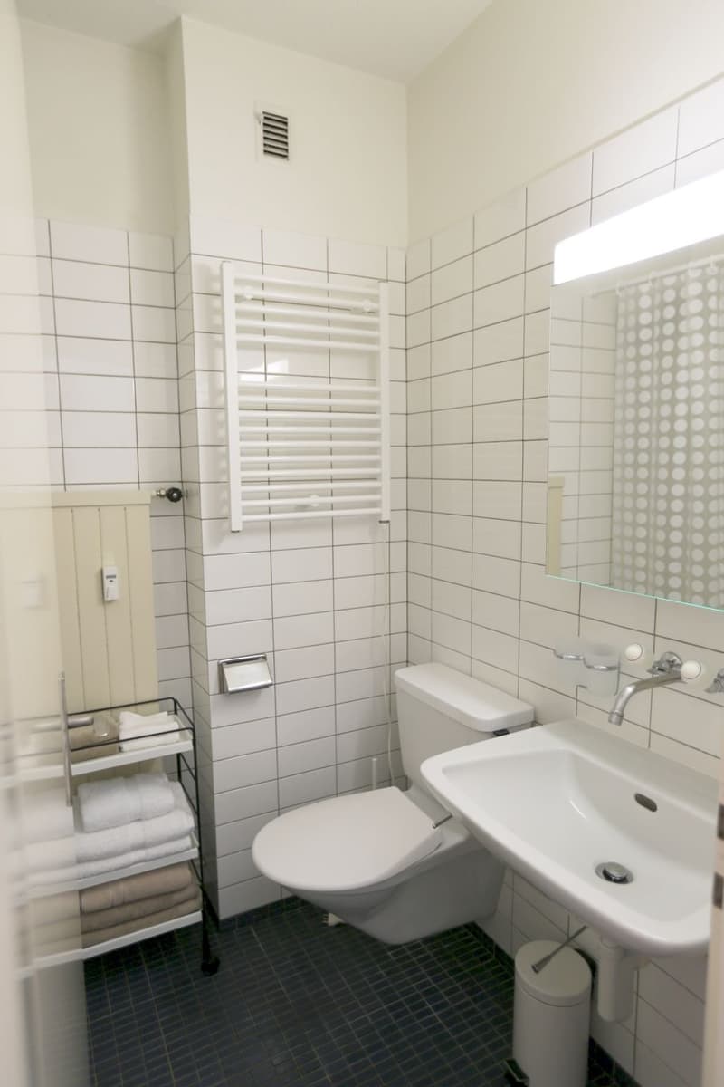 Tiled bathroom with white walls, toilet, sink, towel rack, and a private washing machine.