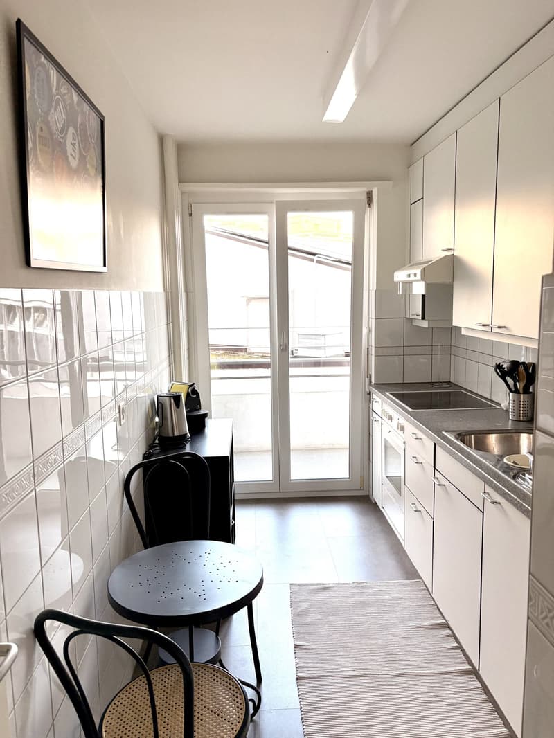 Kitchen with table and chairs, stove, sink, refrigerator, cabinets, double sliding doors to balcony, tile walls, ceiling lamp, painting