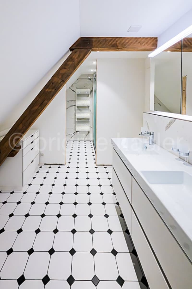 Spacious bathroom with white walls, black and white octagonal tile flooring, a large vanity with a sink, and a towel warmer on the wall.