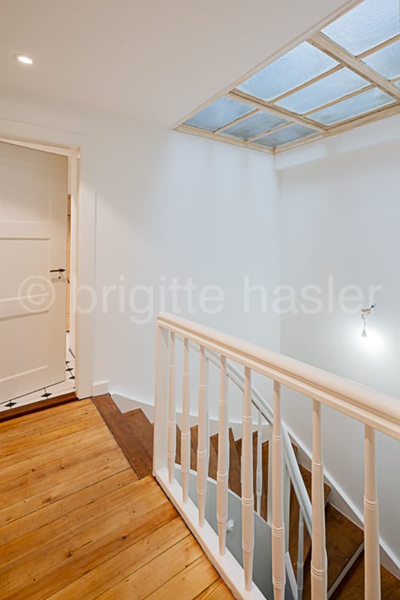 Wooden staircase with white railing leading to a skylight above, providing natural light to the space.