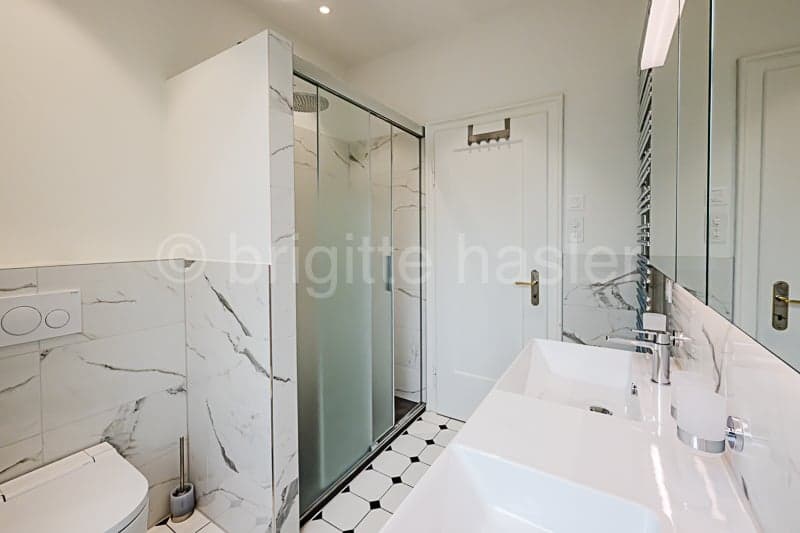 Spacious bathroom with marble-like tiles, glass shower enclosure, vanity sink, and white fixtures