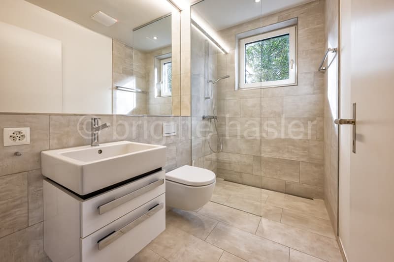 modern bathroom with white sink, white toilet, glass shower enclosure, beige tiles, mirror
