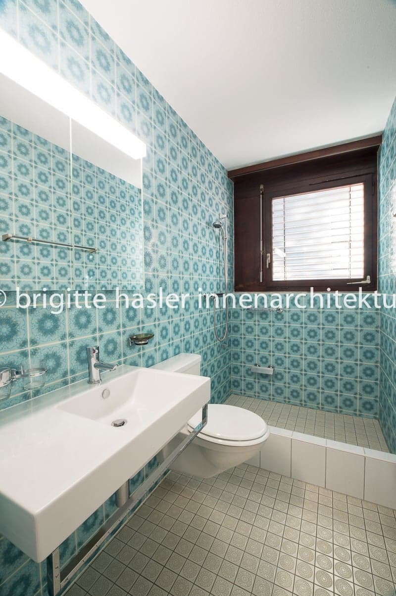 Bathroom with blue tiles, white sink, toilet, shower, and window with blinds