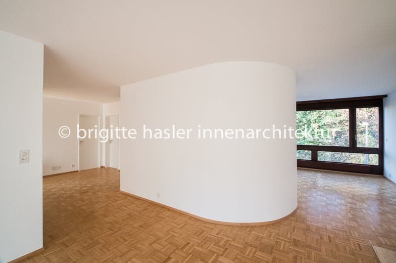 Empty room with wooden floor, white walls, large window, curved wall