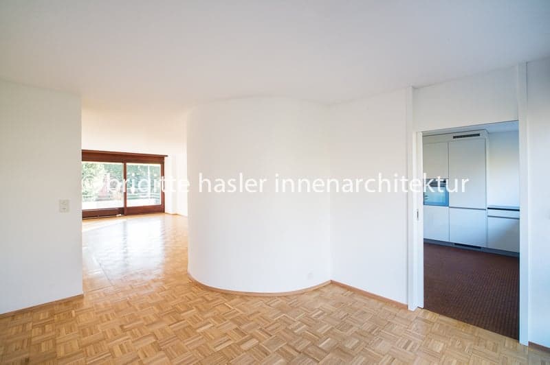 empty room, wooden floor, white walls, large window, open door to kitchen