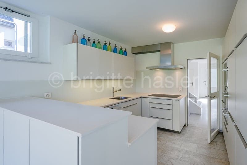 modern kitchen with white cabinets, countertops, and appliances, a sink with a faucet, a stove with an extractor hood, and a window