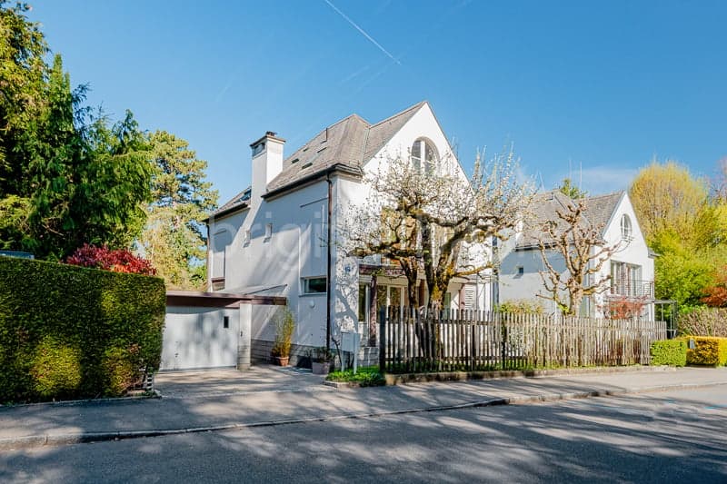 2 story house, white exterior, gray roof, garage, wooden fence, trees, shrubs