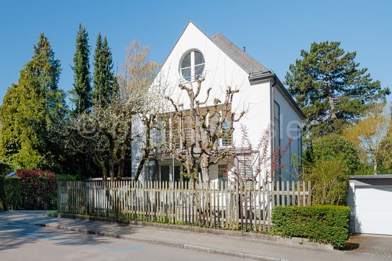 white house, 2 stories, gray roof, wooden fence, balcony, trees, bushes