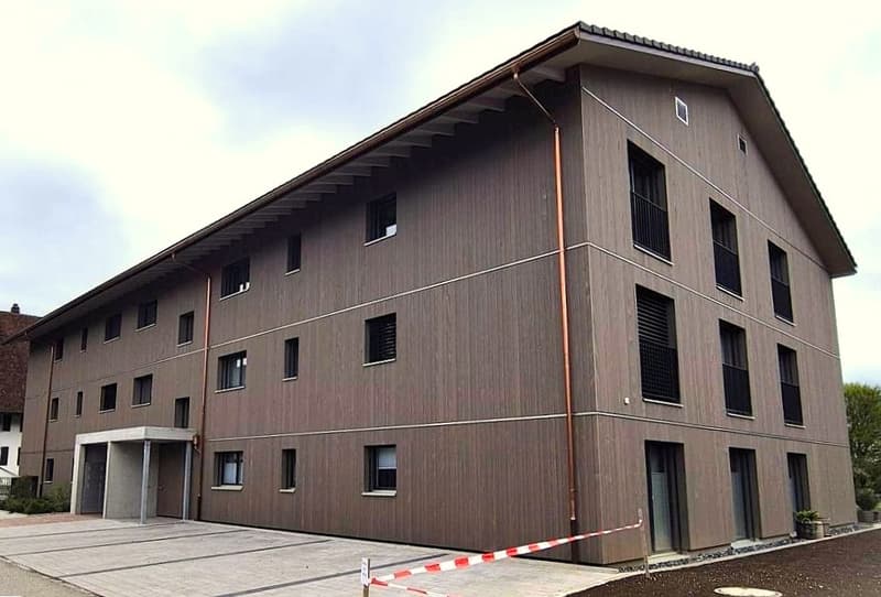 3 story building, brown exterior, multiple windows, parking area