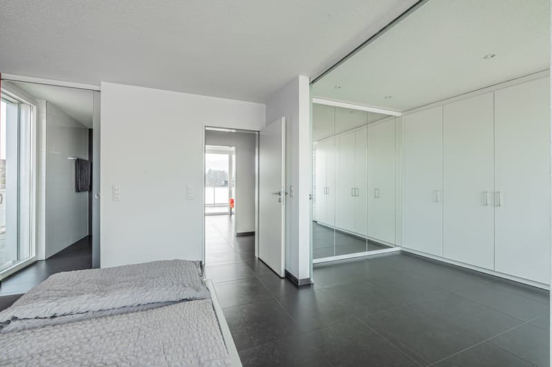modern bedroom with white walls, black tiled floor, large mirror, double bed, and a glass door leading to another room